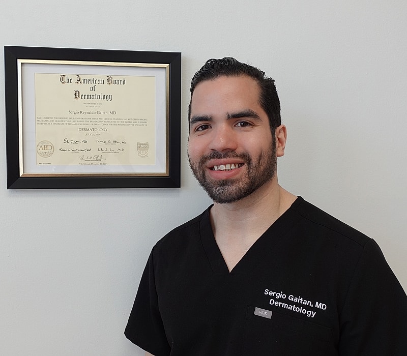 Dermatologist with certification on wall behind.